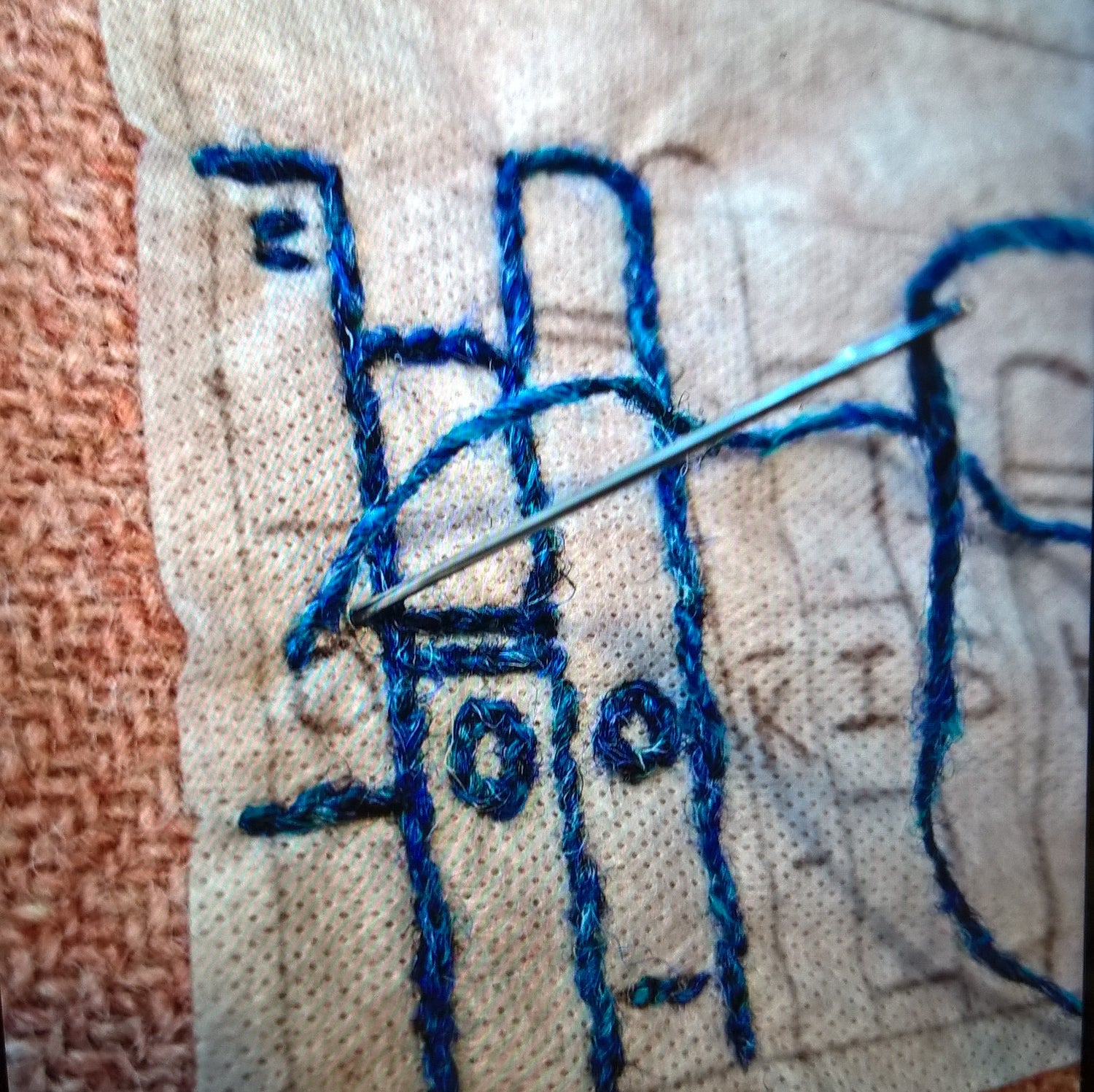 Hand embroidering with blue thread on Harris Tweed fabric, close-up view