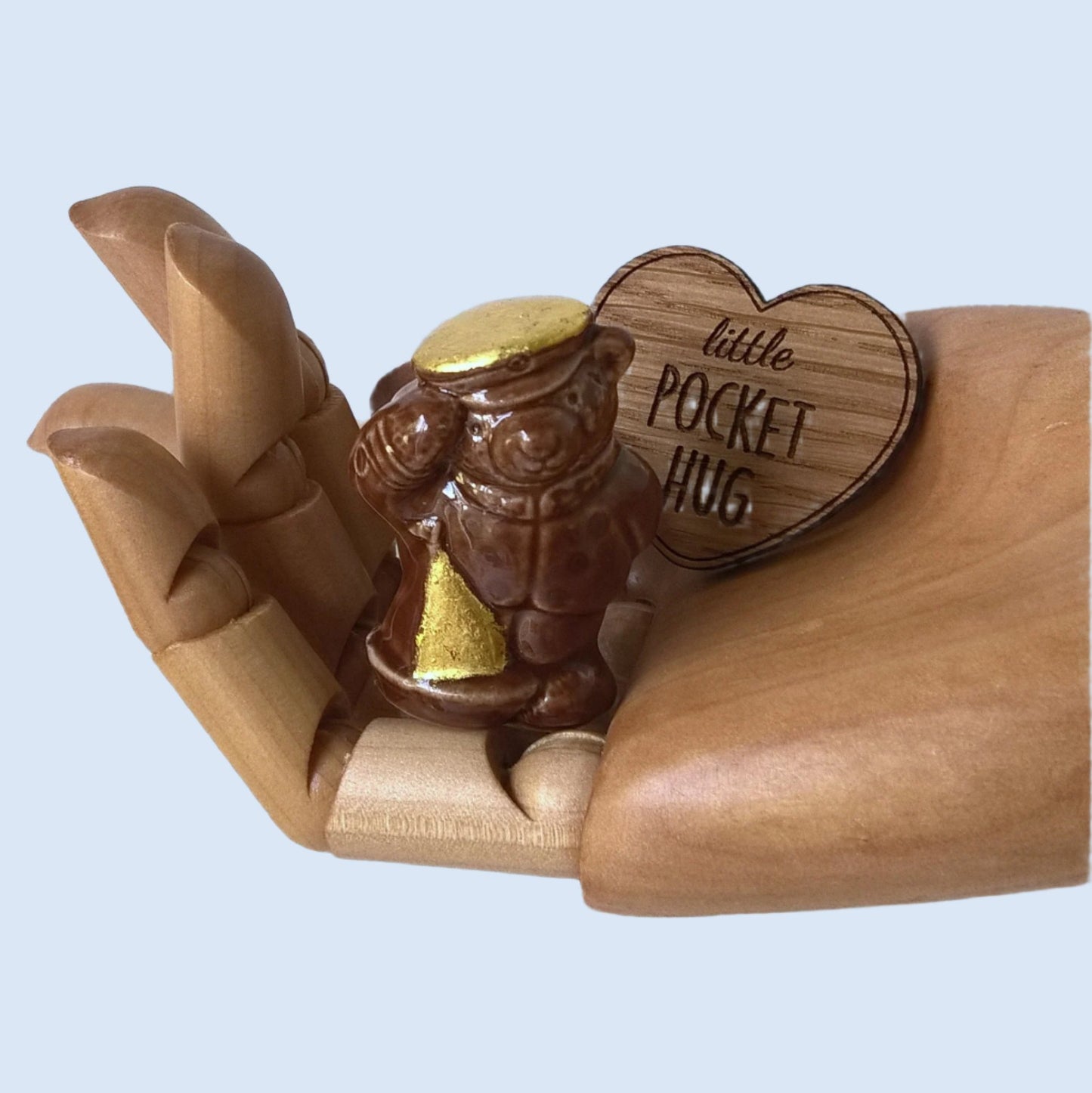Miniature brown ceramic sailor bear fits into the palm of a hand, along with the wooden heart pocket hug 